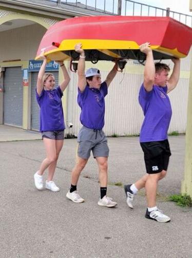 Three students carry a boat over their heads through Eldridge Park.